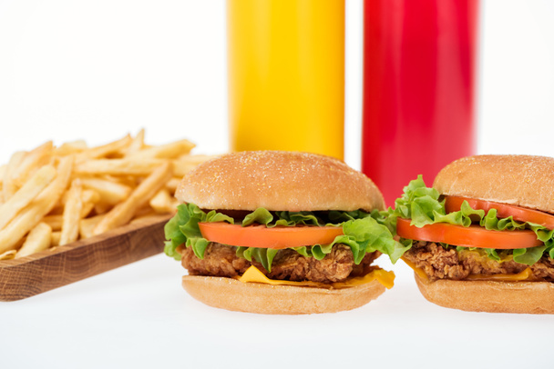 selective focus of tasty chicken burgers near french fries and bottles isolated on white - Photo, Image