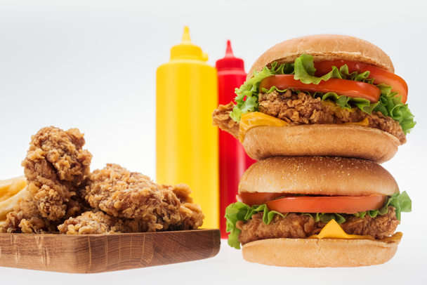 messa a fuoco selettiva di croccanti pepite di pollo e hamburger di pollo vicino a bottiglie con ketchup e senape isolati su bianco
 - Foto, immagini