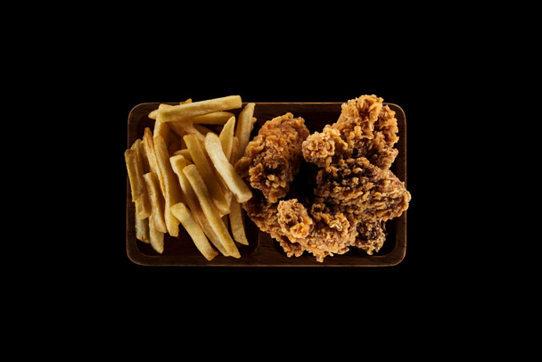 vista superior de sabrosas papas fritas y nuggets de pollo en plato aislado en negro
 - Foto, Imagen