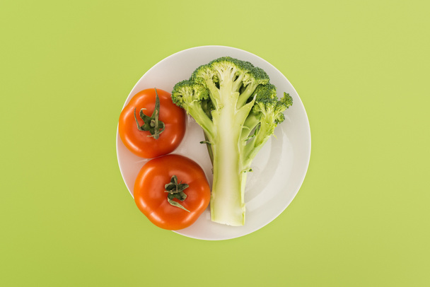 top view of red tomatoes near organic broccoli on white plate isolated on green - Photo, Image