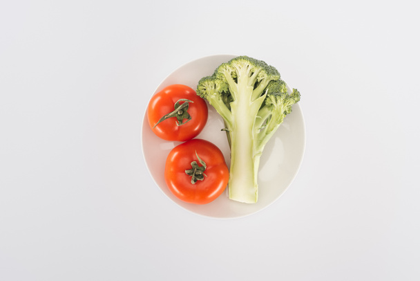 top view of red tomatoes near organic broccoli on plate isolated on white - Foto, Imagem