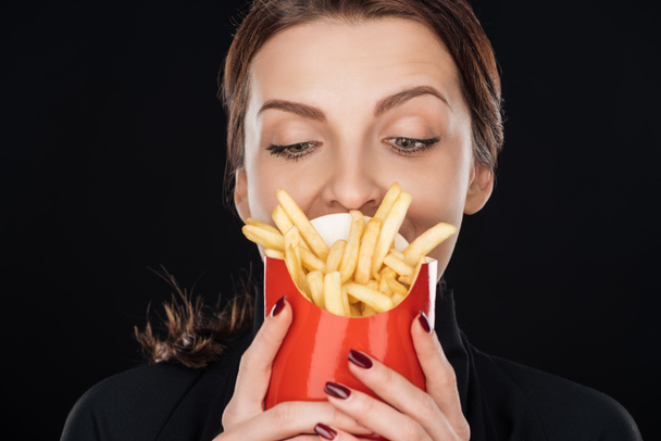 woman looking at french fries isolated on black - Фото, изображение