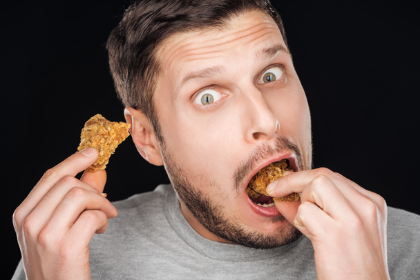 emotional man eating tasty chicken nuggets while looking at camera isolated on black - Φωτογραφία, εικόνα