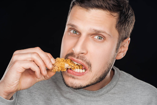 man eating crispy chicken nugget while looking at camera isolated on black - Фото, зображення