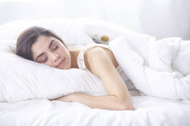 Прекрасная молодая женщина греется в постели по утрам. Красивое лицо модели выглядит сексуально в камере
 - Фото, изображение