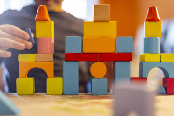 een kind speelt met gekleurde houten blokken op home.kid speelt en bouwt gebouwen en torens met gekleurde houten blokken. - Foto, afbeelding
