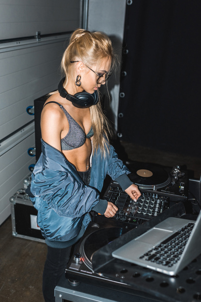 attractive dj woman standing in headphones while touching dj mixer  - Photo, Image