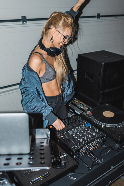 glückliche DJ-Frau mit Kopfhörer, Hand über dem Kopf und berührendem DJ-Mischpult - Foto, Bild