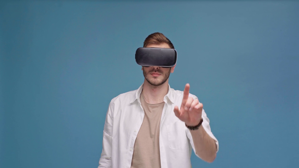 man in virtual reality headset pointing with finger at camera isolated on blue with copy space - Materiał filmowy, wideo