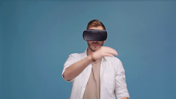 man in virtual reality headset doing swiping gestures and pointing with finger isolated on blue - Materiał filmowy, wideo