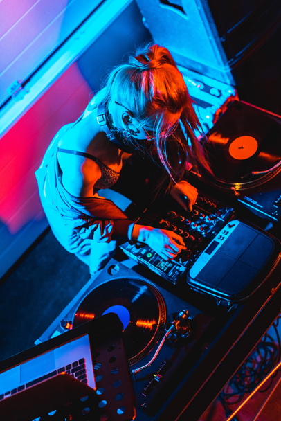 bovenaanzicht van blonde dj meisje aanraken van dj mixer in nachtclub - Foto, afbeelding