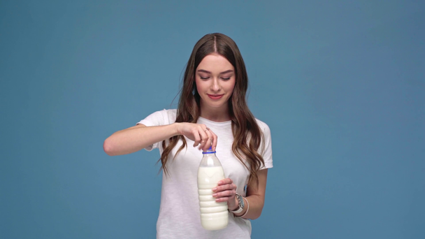 güzel kız kamera, gülümseyen ve mavi izole süt şişe açılış bakarak - Video, Çekim