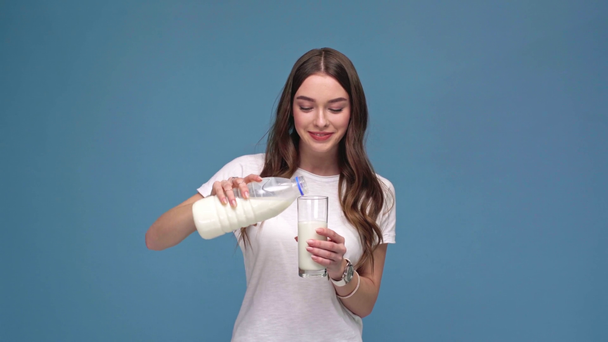 bella ragazza versando il latte, sorridente, guardando la fotocamera e mostrando vetro alla fotocamera isolata su blu
 - Filmati, video