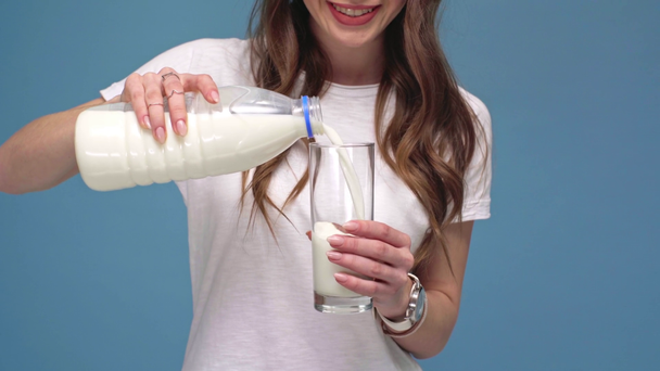 abgeschnittene Ansicht eines Mädchens, das Milch gießt, lächelt und Glas in die Kamera zeigt, isoliert auf blau - Filmmaterial, Video