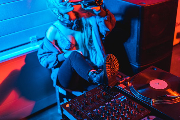 selektiver Fokus von DJ-Mixer und Schallplatte mit DJ-Frau, die aus Flasche im Hintergrund trinkt - Foto, Bild