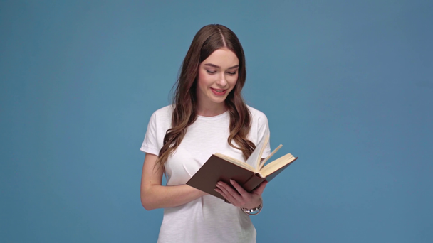 beautifu lächelndes Mädchen blättert Seiten und liest Buch isoliert auf blau - Filmmaterial, Video