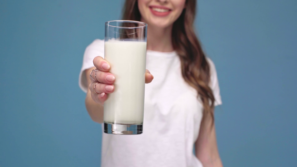 abgeschnittene Ansicht eines Mädchens, das ein Glas Milch in die Kamera hält und isoliert auf blau lächelt - Filmmaterial, Video