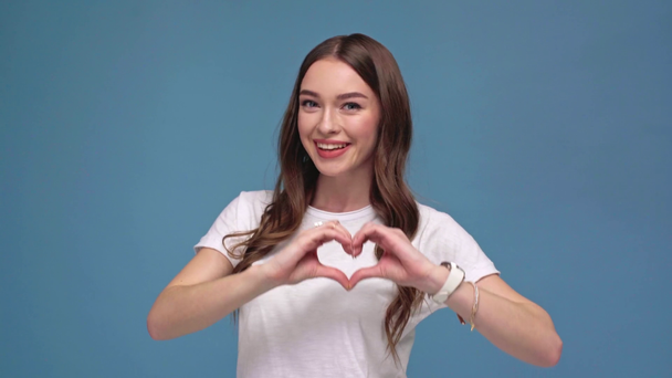 hermosa chica sonriente mostrando el signo en forma de corazón hecho con las manos y mirando a la cámara aislada en azul
 - Metraje, vídeo