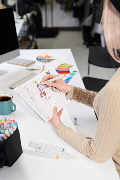 Σχεδιαστής μόδας κάθεται στο τραπέζι και σχεδιάζοντας τα ρούχα σκίτσο στο γραφείο - Φωτογραφία, εικόνα