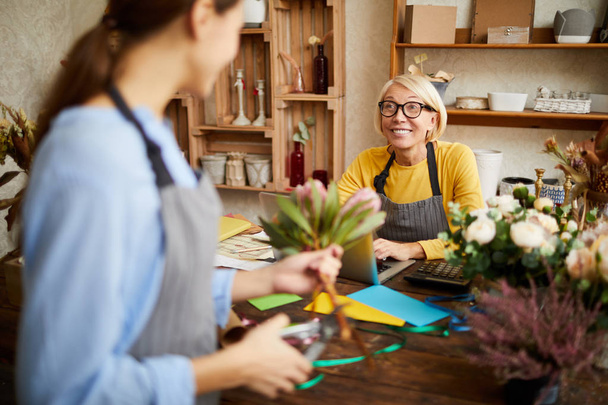 Portrait of mature flower shop owner talking to florist and smiling, copy space - Photo, Image