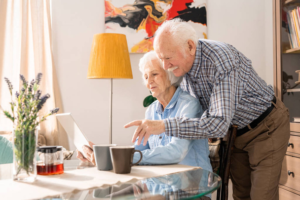 Вид сбоку портрет современной пожилой пары с помощью ноутбука дома во время онлайн-покупок вместе, копировать пространство
 - Фото, изображение