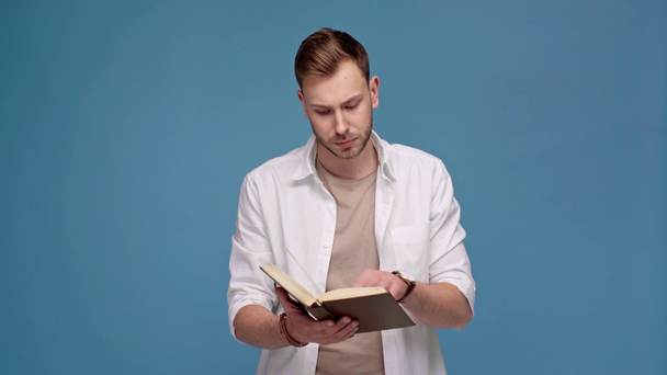 komea mies kääntää sivuja ja lukeminen kirja eristetty sininen
 - Materiaali, video