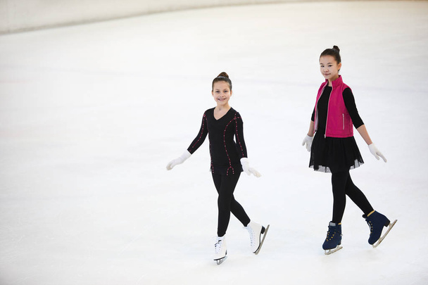 Retrato de alto ángulo de dos niñas patinaje artístico en pista de hielo y sonriendo felizmente, espacio de copia
 - Foto, imagen