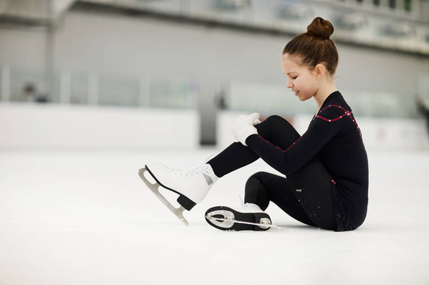 Vista laterale ritratto della bambina ferita nella pista di pattinaggio strofinando ginocchio seduto sul ghiaccio, copiare spazio
 - Foto, immagini