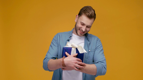 happy handsome man hugging gift box and looking at camera isolated on yellow - Filmmaterial, Video