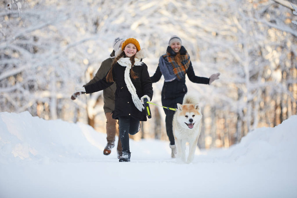 Full length portrait of happy girl walking dog in beautiful winter park, copy space - Photo, Image