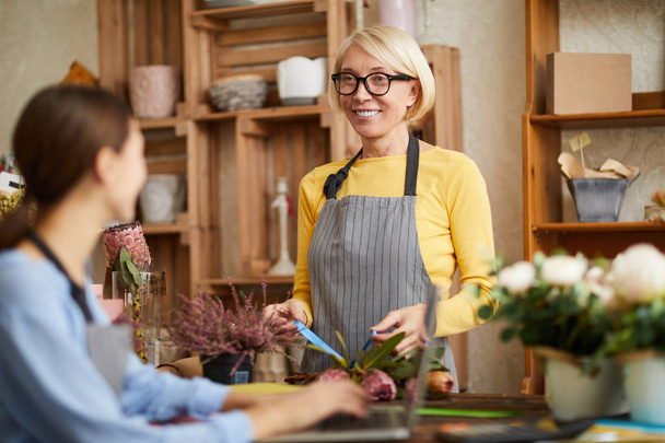 Талия портрет зрелого владельца цветочного магазина разговаривая с работником и улыбаясь, копировать пространство
 - Фото, изображение