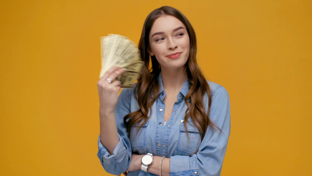 mooi meisje kijken camera, zwaaien dollar biljetten en glimlachend geïsoleerd op geel - Video
