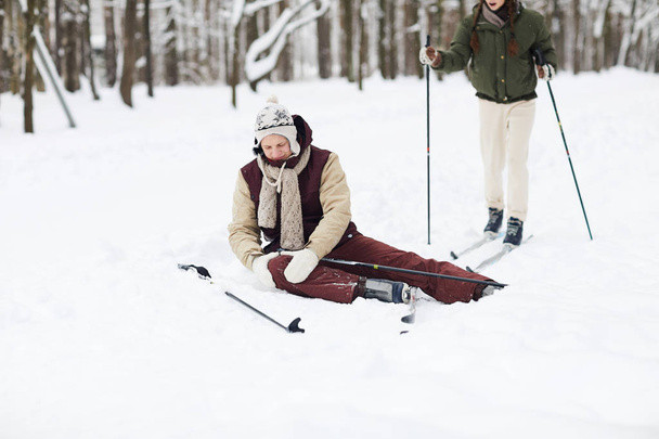 Ganzkörperporträt eines verletzten jungen Mannes, der beim Skifahren verletzt auf Schnee sitzt, Kopierraum - Foto, Bild