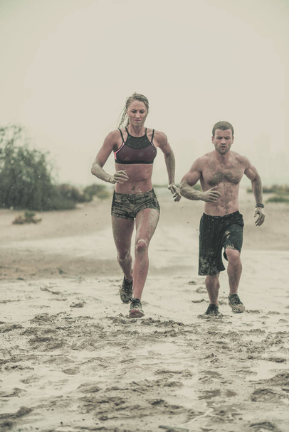 М'язистий чоловік і жінка-спортсмен, покритий брудом, біжить по нерівній місцевості з пустельним тлом в екстремальній спортивній гонці з гранжевою текстурованою обробкою
 - Фото, зображення