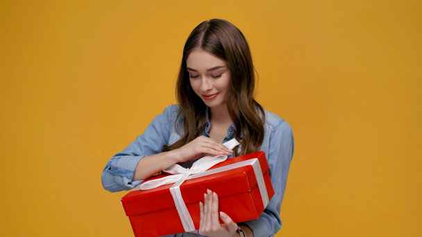 güzel gülümseyen kız okşayarak ve sarı izole hediye kutusu sarılma kameraya bakıyor - Video, Çekim