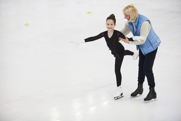 Retrato completo del entrenador senior ayudando a la niña a patinar en la pista de patinaje artístico, espacio para copiar
 - Foto, Imagen