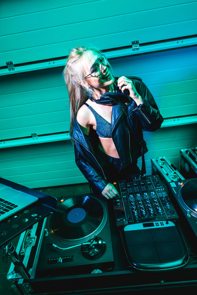 sonriente dj mujer en auriculares de pie cerca de equipo en discoteca
 - Foto, Imagen