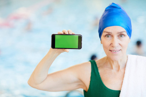 Retrato de la mujer mayor activa en la piscina que presenta la aplicación móvil, espacio de copia
 - Foto, Imagen