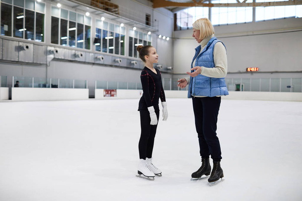 Полнометражный портрет взрослой женщины-тренера, разговаривающей с маленькой девочкой во время тренировки фигурного катания на катке, копировальное пространство
 - Фото, изображение