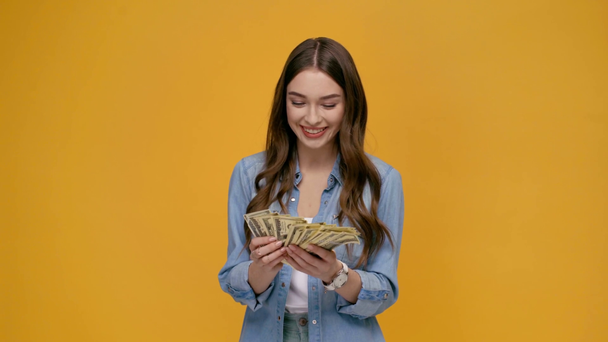 krásná dívka počítání dolarové bankovky, při pohledu na fotoaparát, s úsměvem a ukazovat peníze izolované na žluté - Záběry, video