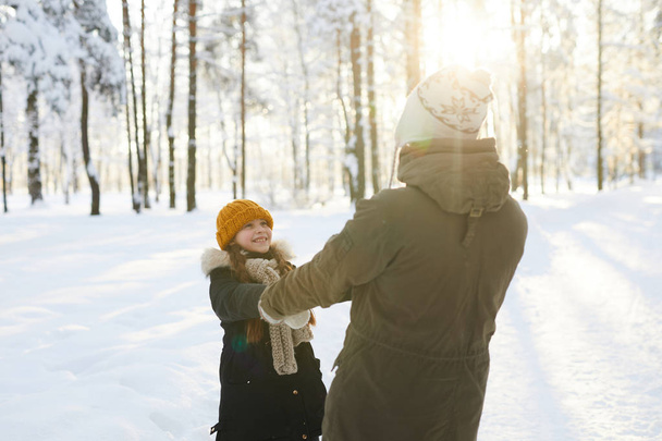Retrato de niña feliz cogida de la mano con papá mientras se divierte en el bosque de invierno iluminado por la luz del sol, espacio de copia
 - Foto, Imagen