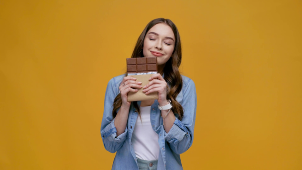 schönes Mädchen, das nach Schokolade riecht, in die Kamera blickt, die Lippe beißt und isoliert auf gelb lächelt - Filmmaterial, Video