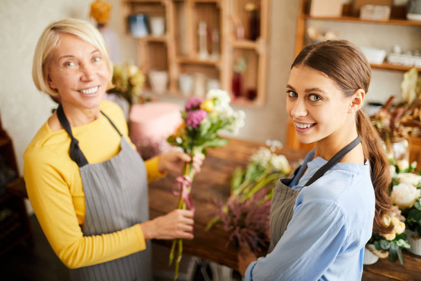 Retrato de ángulo alto de dos floristas femeninas mirando a la cámara y sonriendo mientras trabajan en la florería, espacio para copiar
 - Foto, Imagen