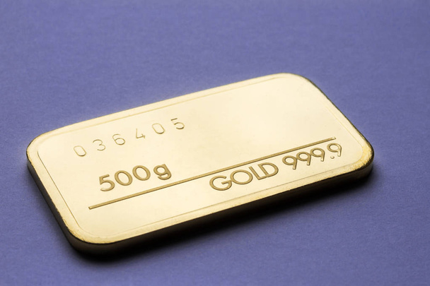 Una barra de oro que pesa 500 gramos sobre un fondo morado. Enfoque selectivo
. - Foto, Imagen