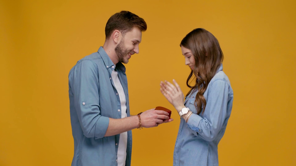 man presenting heart-shaped gift box and embracing happy woman isolated on yellow - Filmagem, Vídeo