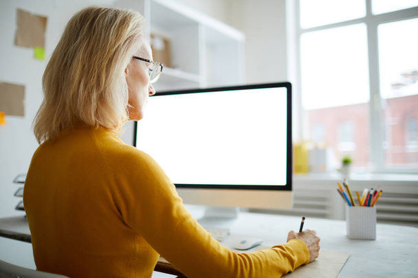 Widok z tyłu portret Dorosła kobieta za pomocą komputera siedząc przy biurku w biurze, miejsce - Zdjęcie, obraz