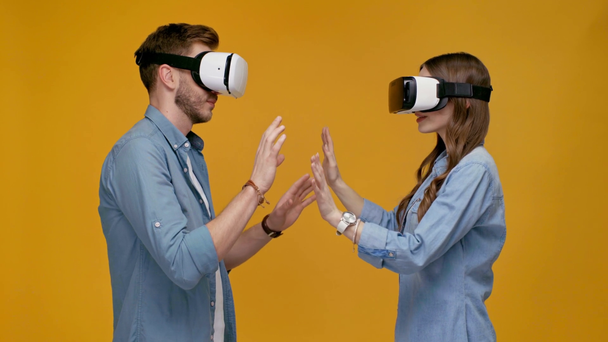άνδρας και γυναίκα στο σετ κεφαλής εικονικής πραγματικότητας χειρονομώ με χέρια απομονωμένες σε κίτρινο - Πλάνα, βίντεο