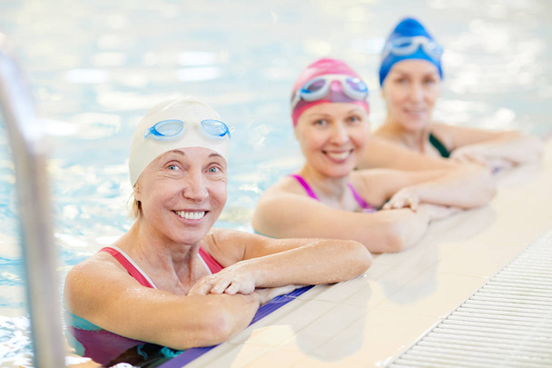 Portrait of three mature women in swimming pool, leaning on border and looking at camera, copy space - Photo, Image