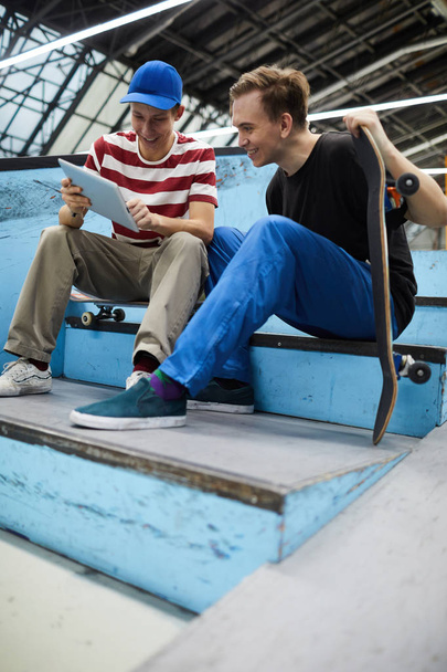 Dos chicos felices en ropa deportiva sentados en la escalera y discutiendo videos en línea o datos sobre trucos de skate
 - Foto, imagen