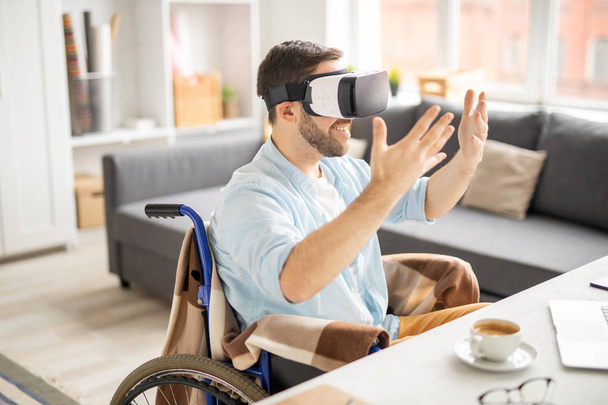 fröhlicher junger Gelegenheitsunternehmer in vr-Brille, der seine Hände vor sich hält, während er etwas Virtuelles betrachtet - Foto, Bild